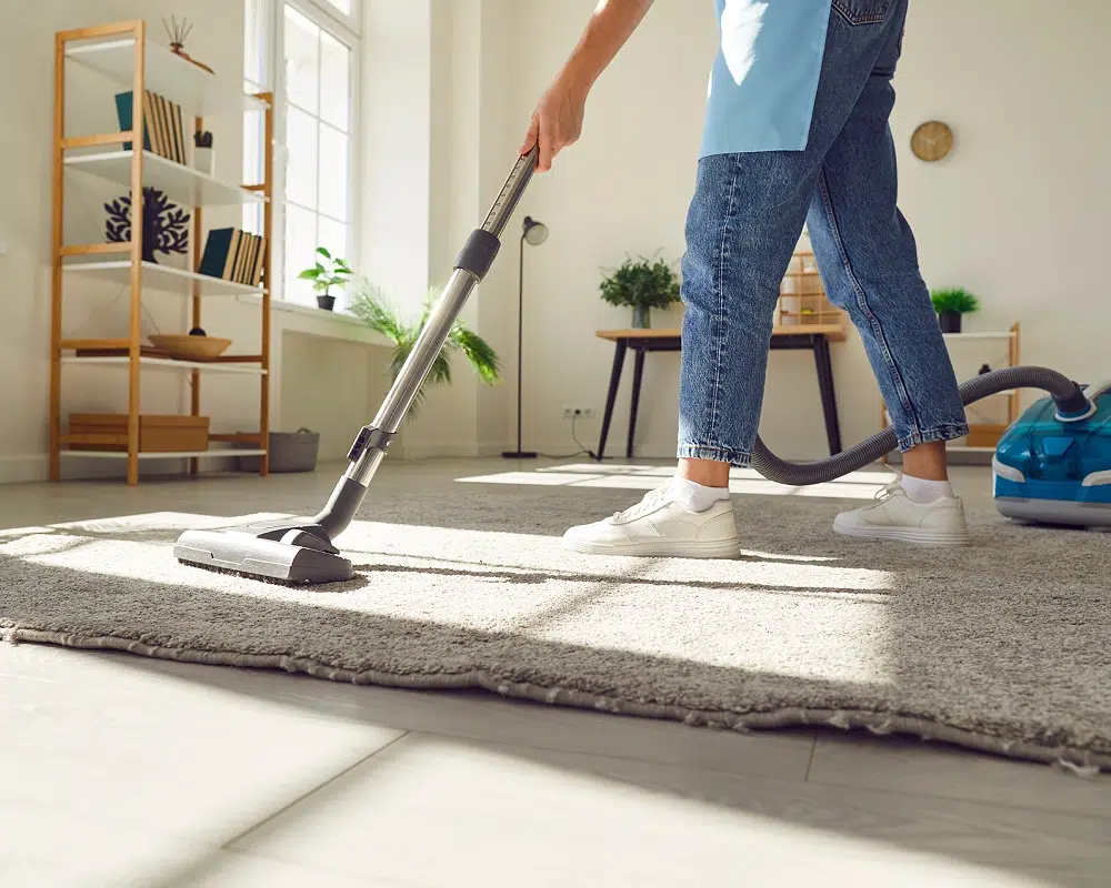 Aspirateur en action dans un salon moderne | ON TIME GROUPE Personne passant l'aspirateur sur un tapis dans un salon lumineux.
